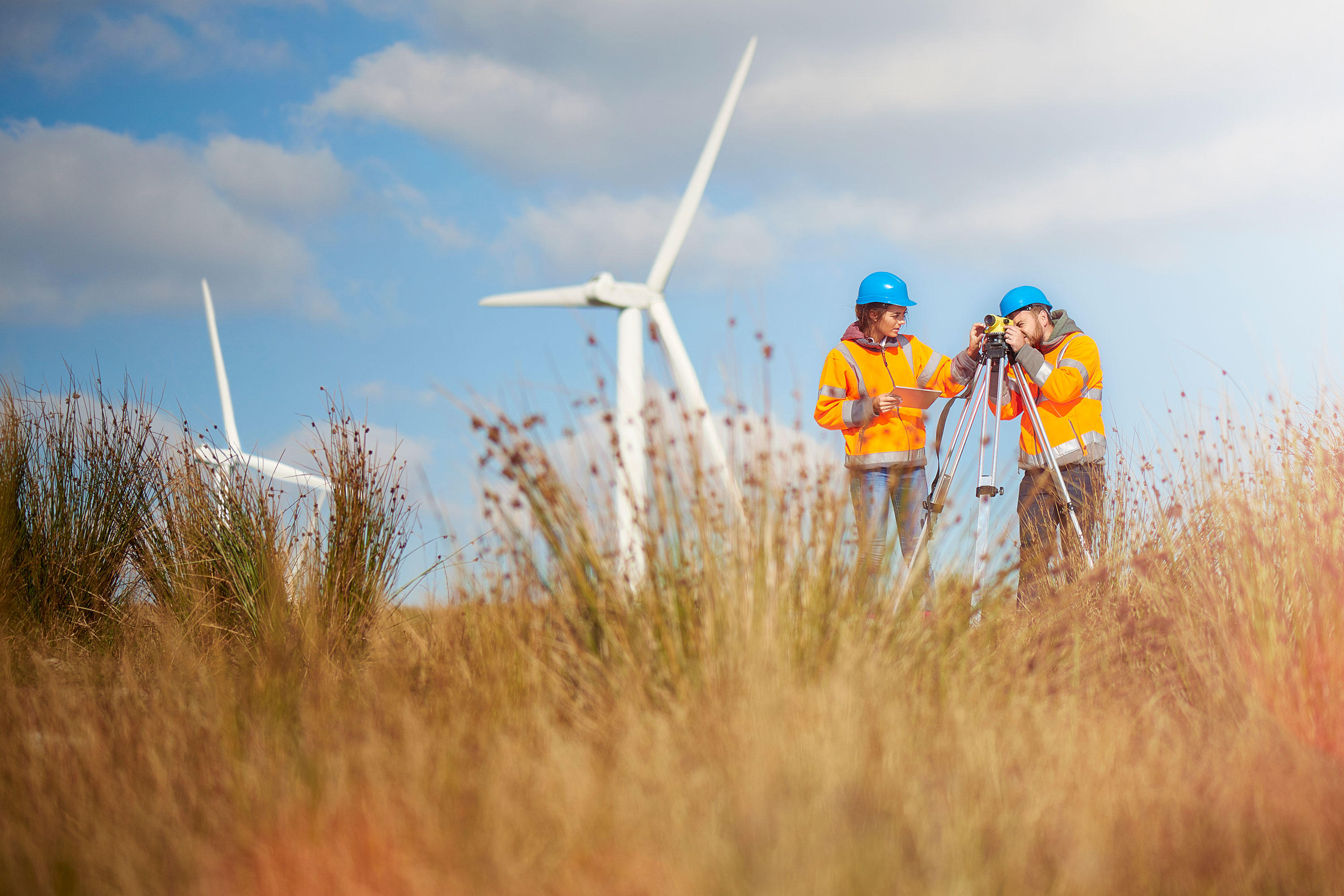 Two individuals stand before a wind turbine in a field